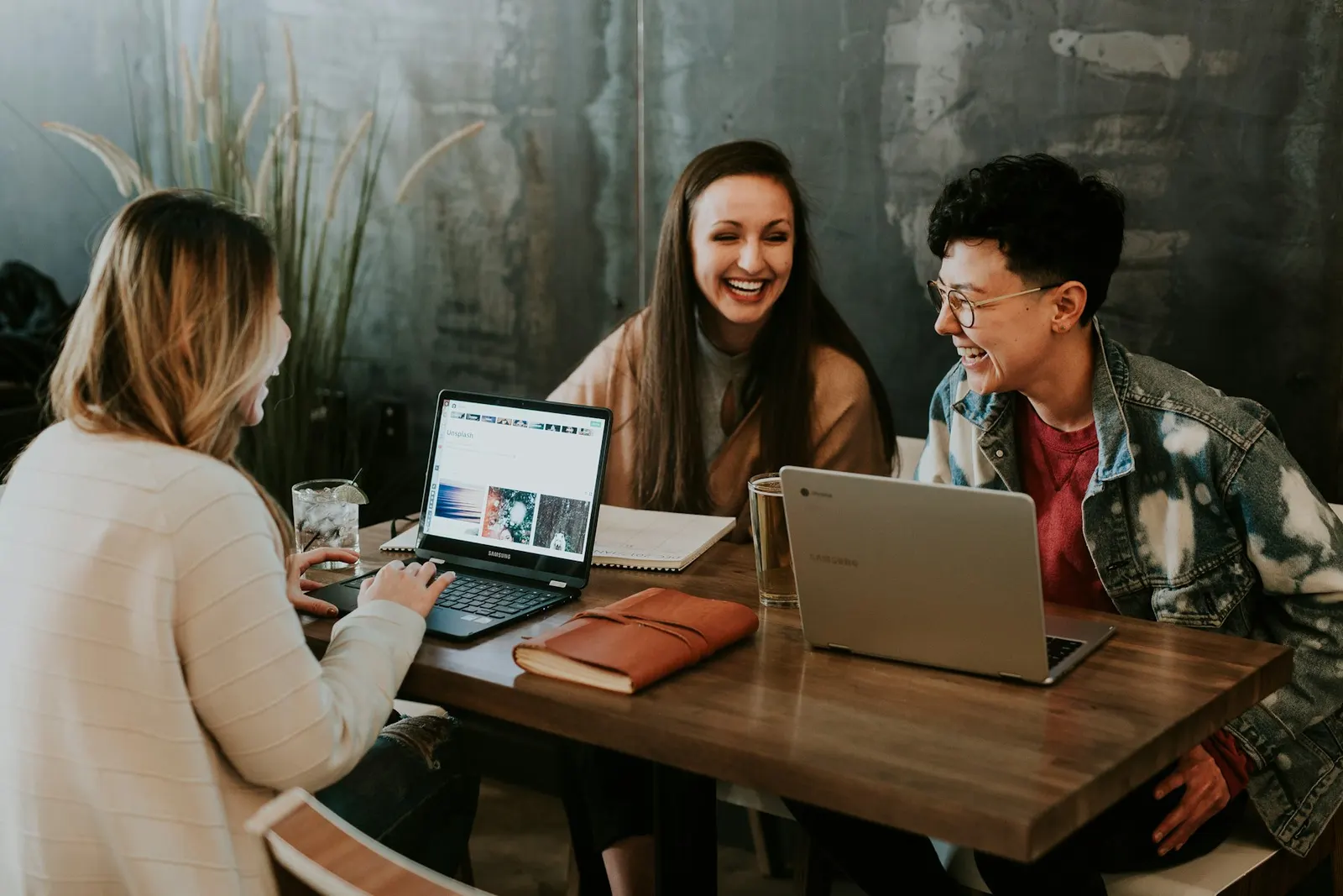 Tres personas del equipo riendo juntas frente a laptops en una mesa de trabajo
