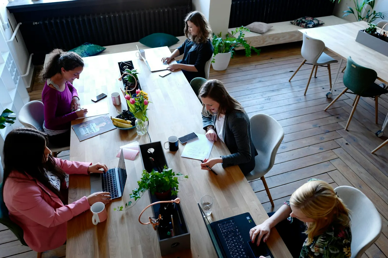 Equipo de personas trabajando juntas en laptops alrededor de una mesa compartida